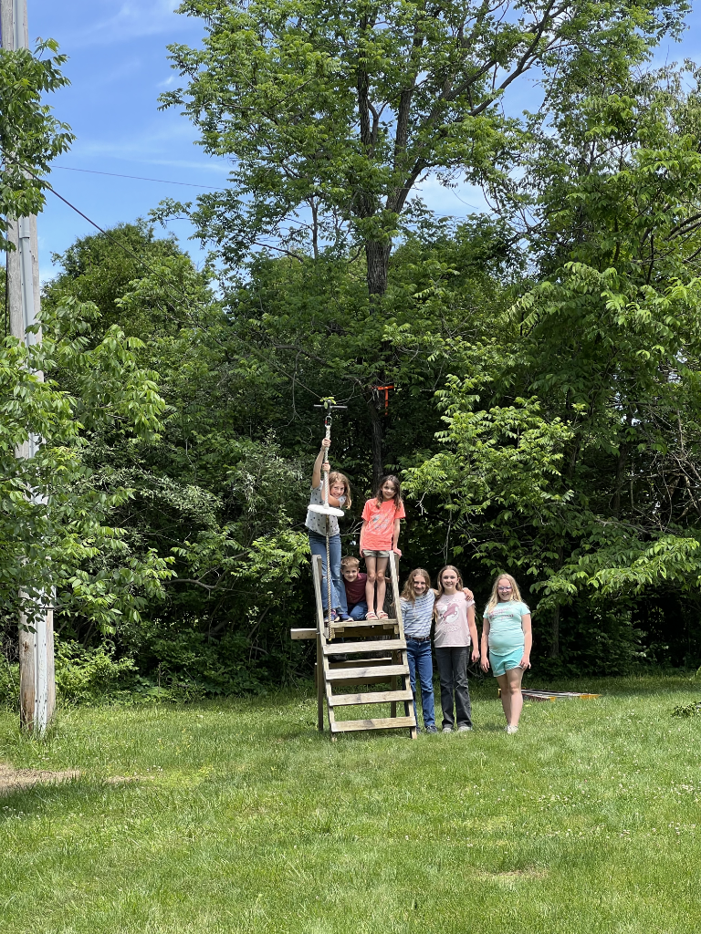 Six grandchildren waiting their turn at the launch platform of a backyard zip line.